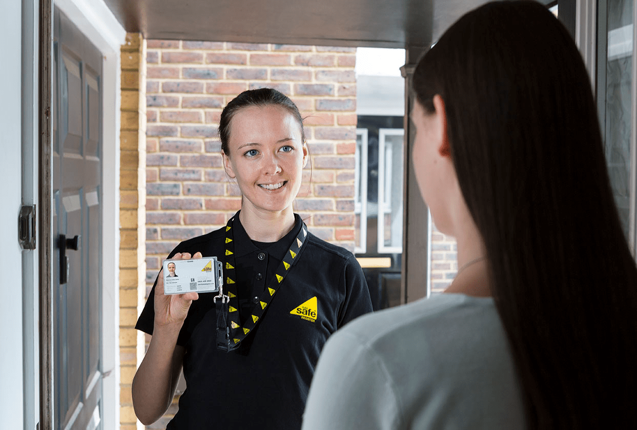 Female gas engineer standing at customer's door showing Gas Safe Register ID card