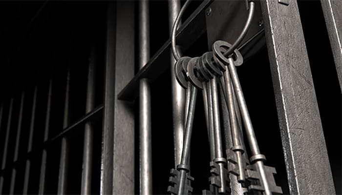 Black and white image of a bunch of keys on jail bars, illustrating a prison sentence